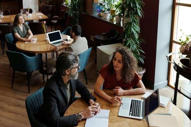 A business owner consulting with a marketing expert in a modern café, discussing strategies with a laptop and notebook on the table.